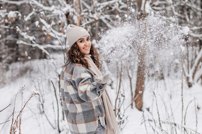 A cute girl walks in a snowy forest, smiles and throws snow