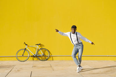 Happy young man dancing in front of yellow wall on sunny day