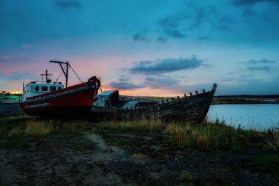 Abandoned boat moored on field against sky during sunset