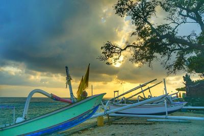 Fishing boats moored on beach against sky during sunset