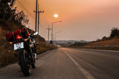 Motorcycle parked on road against sky during sunset