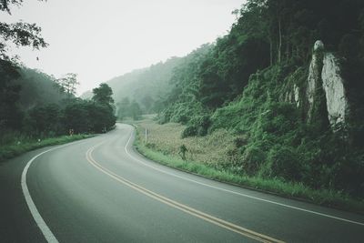 Empty country road along trees and against clear sky