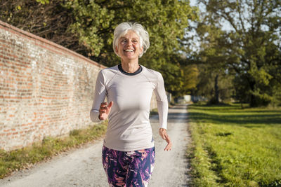 Happy senior woman running along brick wall in a park