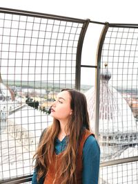 Young woman standing by fence in city