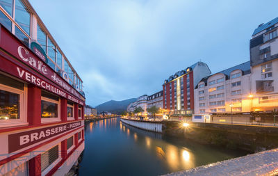 Illuminated bridge over river by buildings against sky at dusk