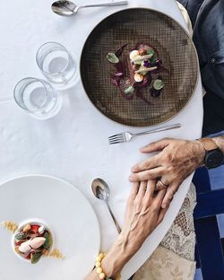 High angle view of senior couple holding hands at table while having food