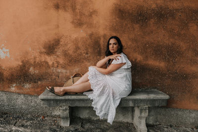 Beautiful young woman sitting on stone bench in front of old orange building