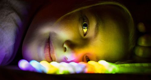 Close-up portrait of young woman lying by colorful illuminated lighting equipment