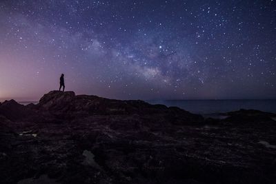 Silhouette young man standing on rock by sea against star field at night