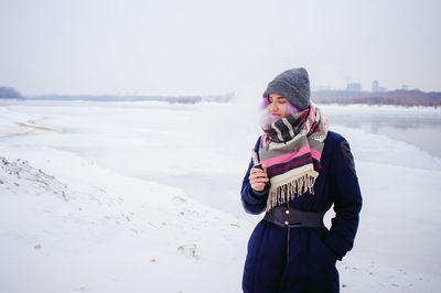 Young woman using phone while standing on snow covered landscape