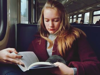 Mid adult woman reading book in bus