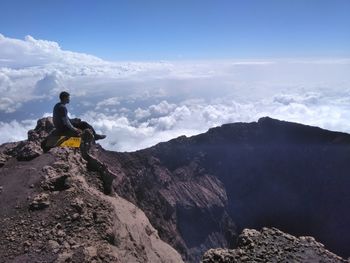 Man sitting on mountain against sky