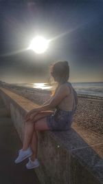 Woman sitting on beach against sky during sunset