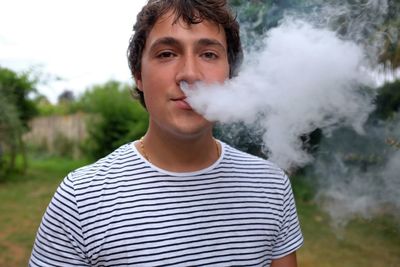 Portrait of man exhaling smoke against trees