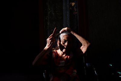 Senior woman combing hair while sitting in darkroom