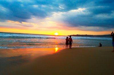 Silhouette people on beach against sky during sunset