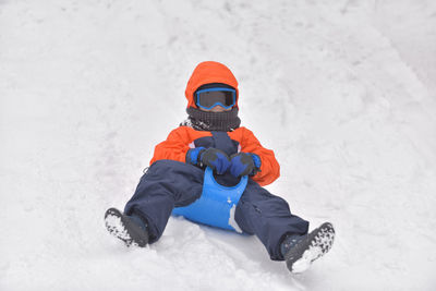 Full length of boy tobogganing on snowy field