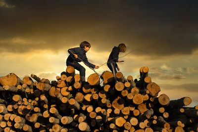 Two kids walking on log against sky during sunset