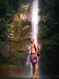Full length of woman standing on rock against waterfall