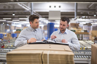 Two men in factory warehouse looking at documents