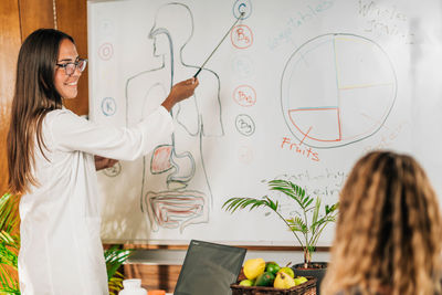 Female nutritionist, standing in front of a white board, explaining the importance of vitamin c 