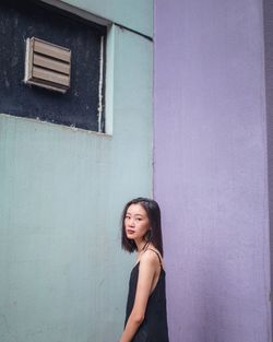 Portrait of smiling young woman standing against wall