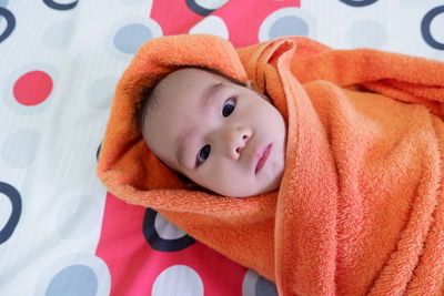 High angle portrait of cute baby wrapped in blanket lying on bed at home