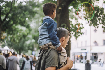 Side view of boy sitting on father's shoulder while shopping at flea market