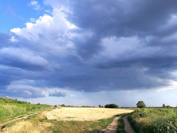 Empty road amidst field against sky