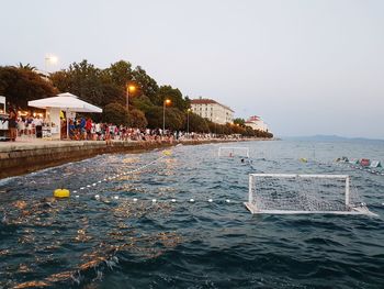 People in swimming pool by sea against clear sky