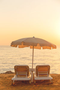 Beige cotton beach umbrella with two sunbeds by the sea against sunny sky. abstract background