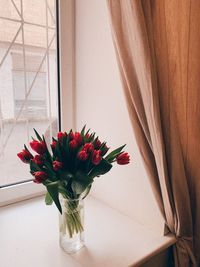 Close-up of red tulips in vase against window
