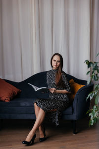 A woman in a dress with polka dots and classic black shoes sits on a dark blue sofa 