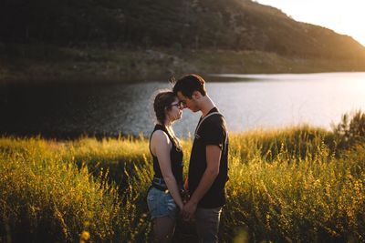 Rear view of couple standing on grass by lake