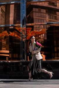 Rear view of woman running in city against glass wall 