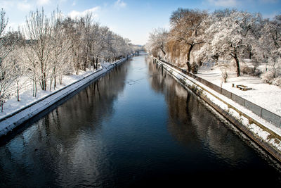 Canal amidst snow covered bare trees at frozen park