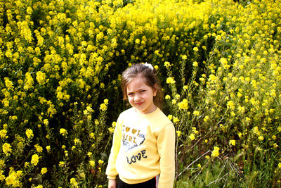 Portrait of girl standing against yellow flowers blooming on field