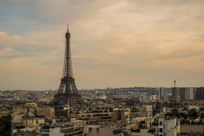 Communications tower in city against sky during sunset