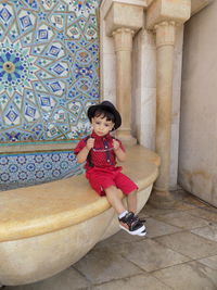 Full length of girl sitting on retaining wall