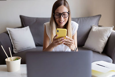 Midsection of woman using mobile phone while sitting on sofa