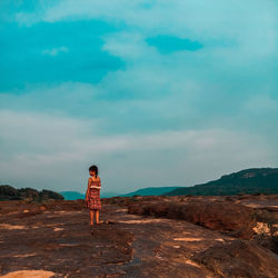 Rear view of girl standing on mountain against sky