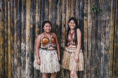 Portrait of a smiling young woman standing against wooden wall