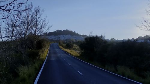 Empty road amidst trees against sky