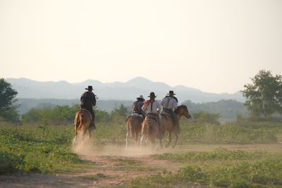 People riding horses on field against sky