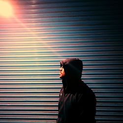 Man wearing hoodie looking away standing against shutter