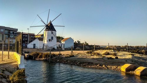 Traditional windmill by river and buildings against sky