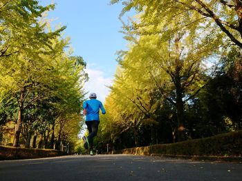 Rear view of man running on footpath amidst trees