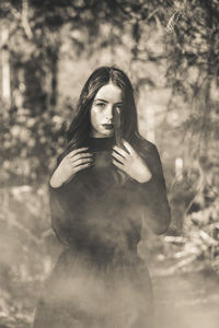 Portrait of young woman standing against trees in forest