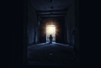 Woman wrapped in blanket sitting at doorway in abandoned building on sunny day