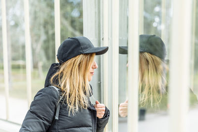 Woman wearing hat standing against window